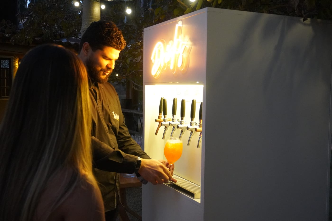 Drink laranja sendo servido no totem E-Drink em um evento ao ar livre, à noite