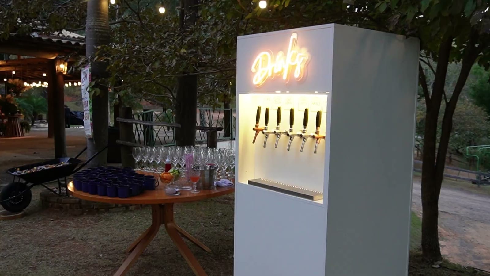 Totem E-Drink montado em um evento ao ar livre, ao lado da mesa de taças
